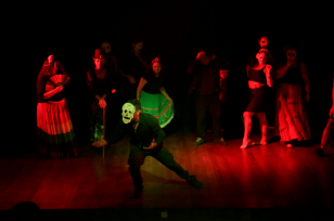 Diversos artistas no palco, encenando uma peça teatral.