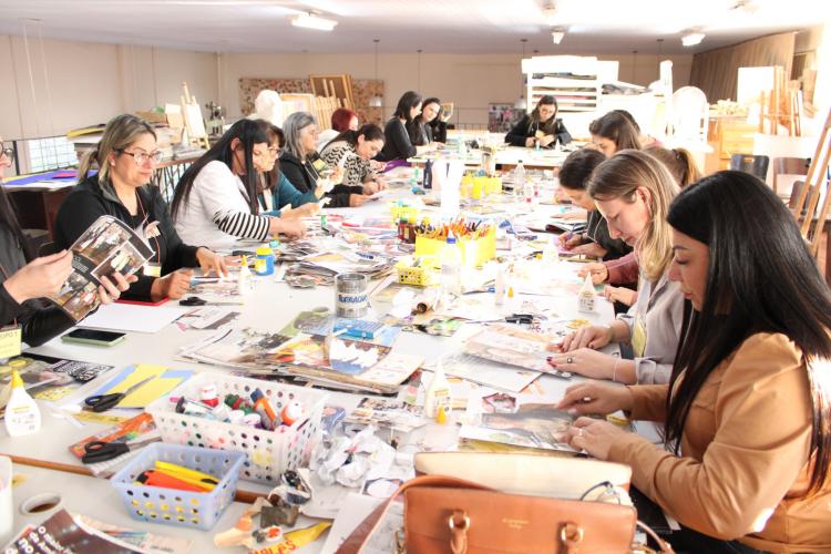 várias pessoas sentadas, recortando e colando fotos de revistas em folhas em branco.