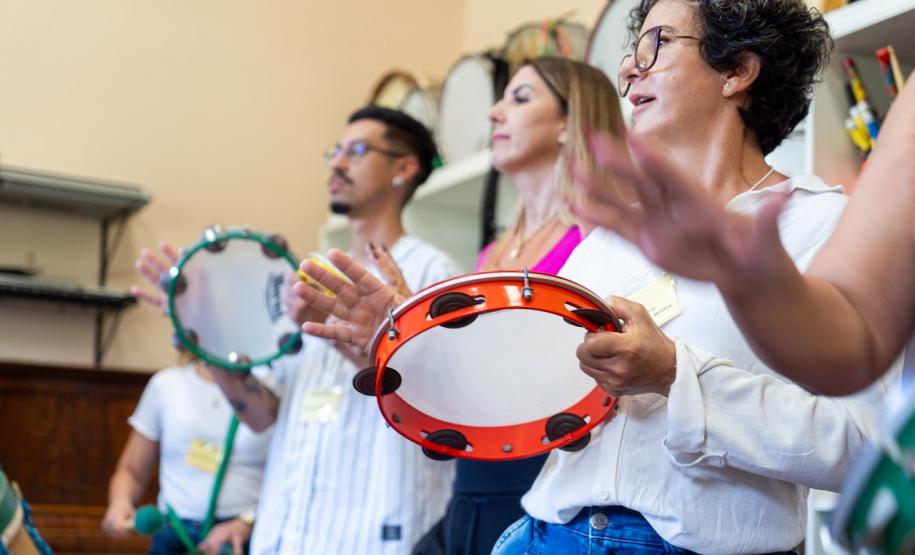 Várias pessoas tocando pandeiro em uma sala.