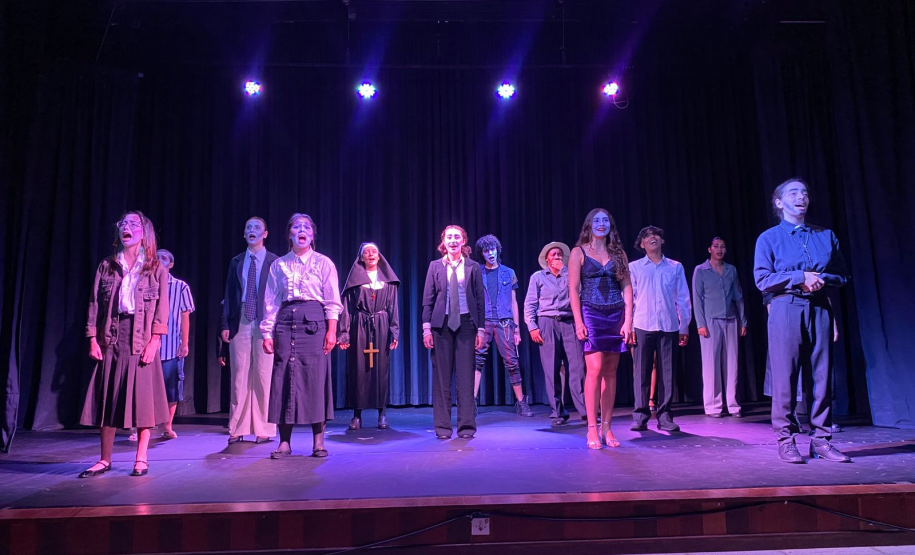 Vários jovens em um palco de teatro, todos de frente para o público.